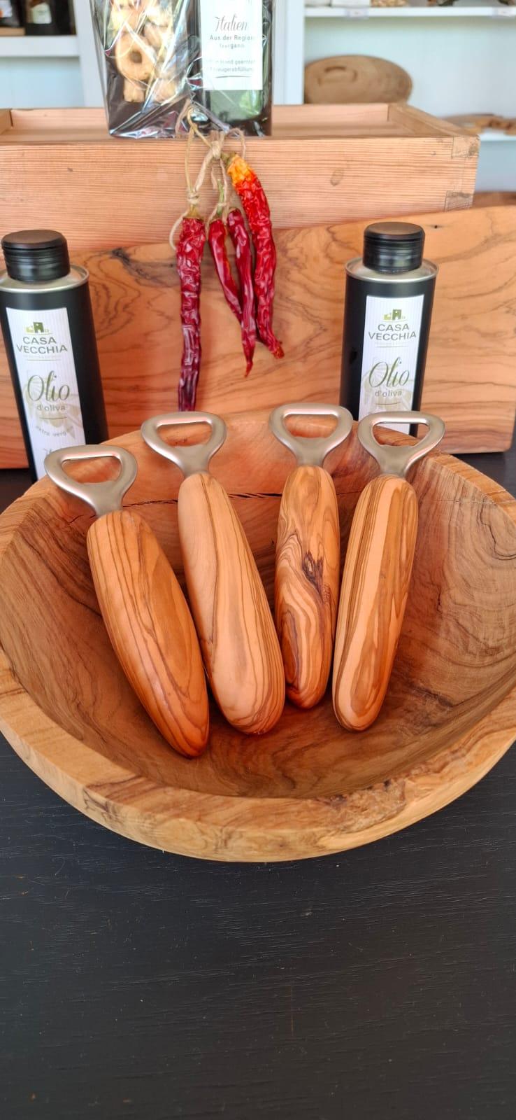 Wooden-handled bottle openers arranged in a wooden bowl with olive oil bottles and hanging peppers in the background.